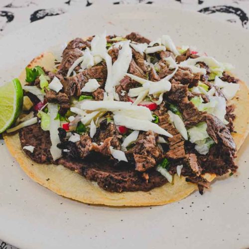 Crisp corn tortillas, topped with refried beans, carne asada, salad vegetables and Oaxacan cheese