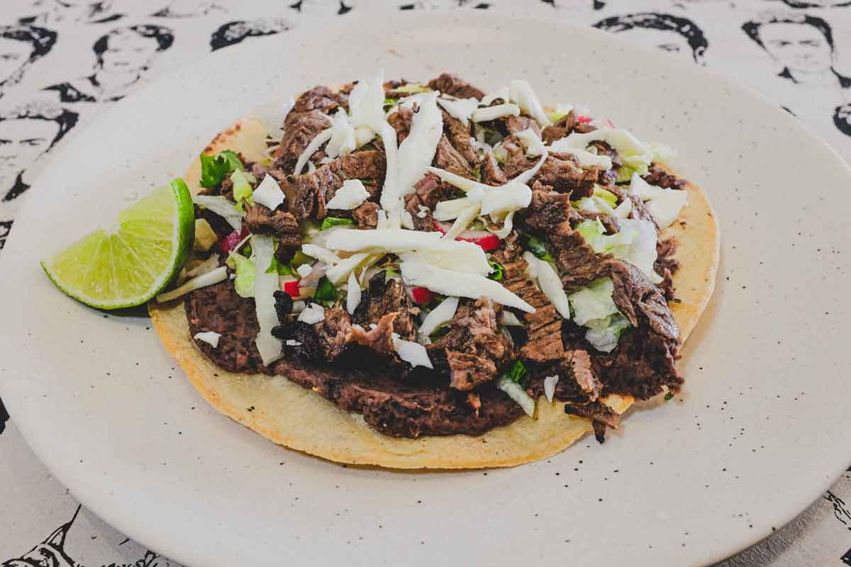 Crisp corn tortillas, topped with refried beans, carne asada, salad vegetables and Oaxacan cheese