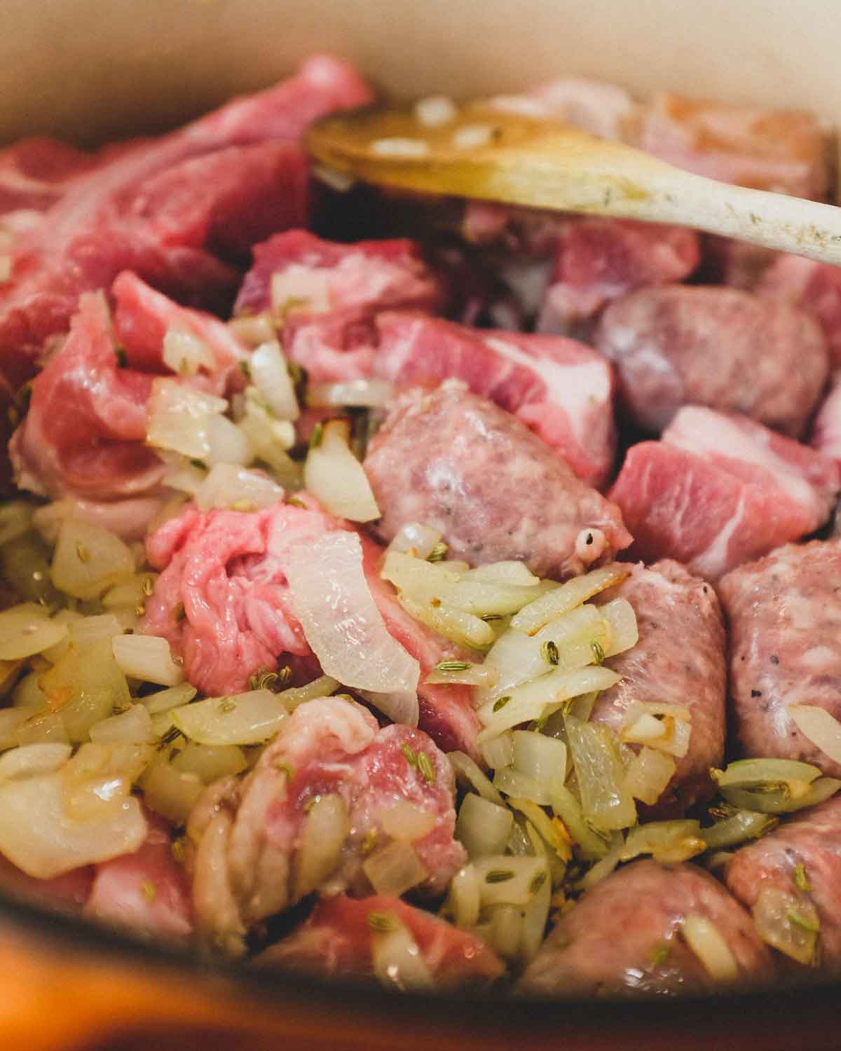 Sausage and pork frying in a large pan with onion and herbs