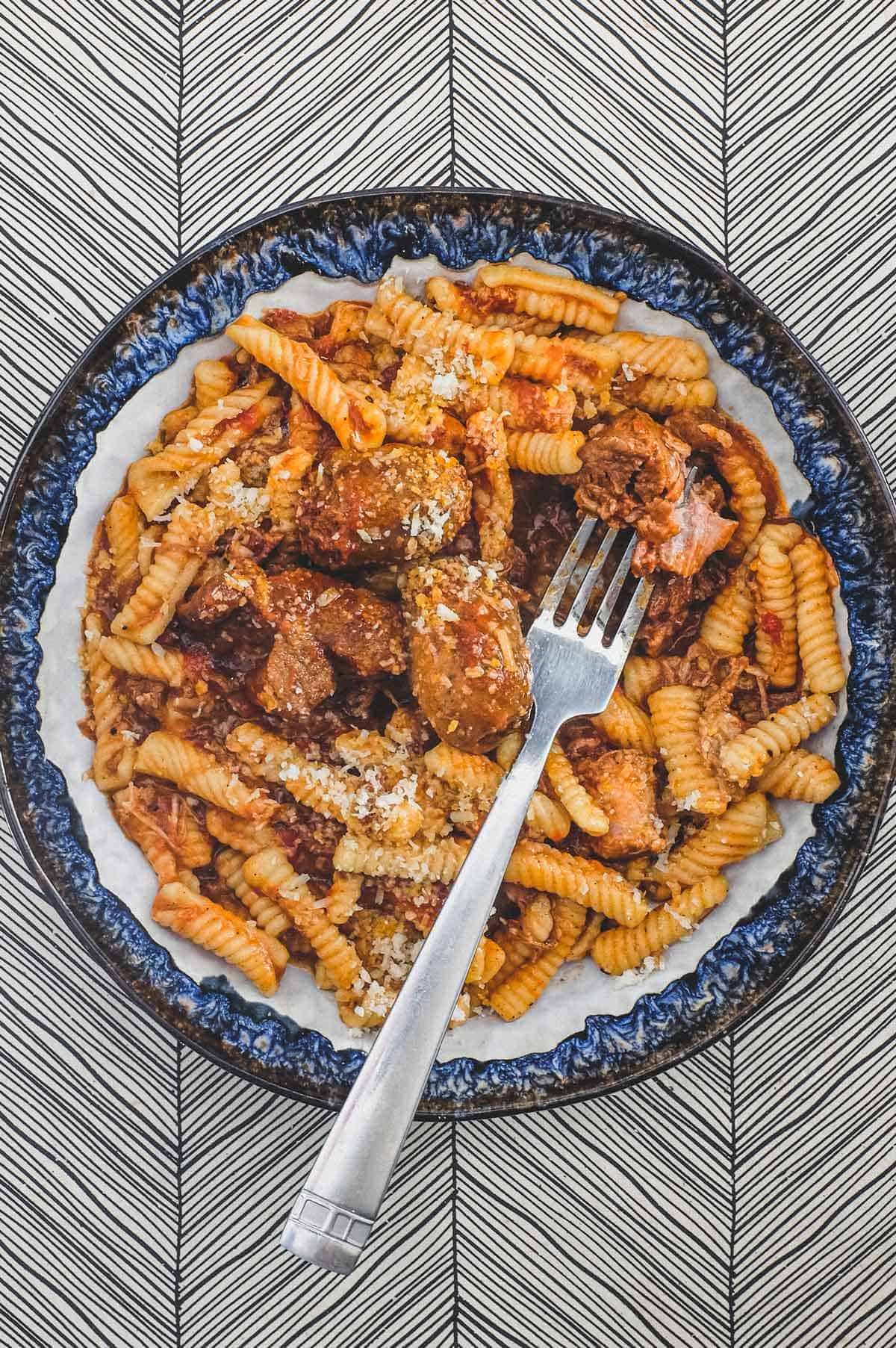 A bowl of cavatelli pasta with pork ragù with a fork