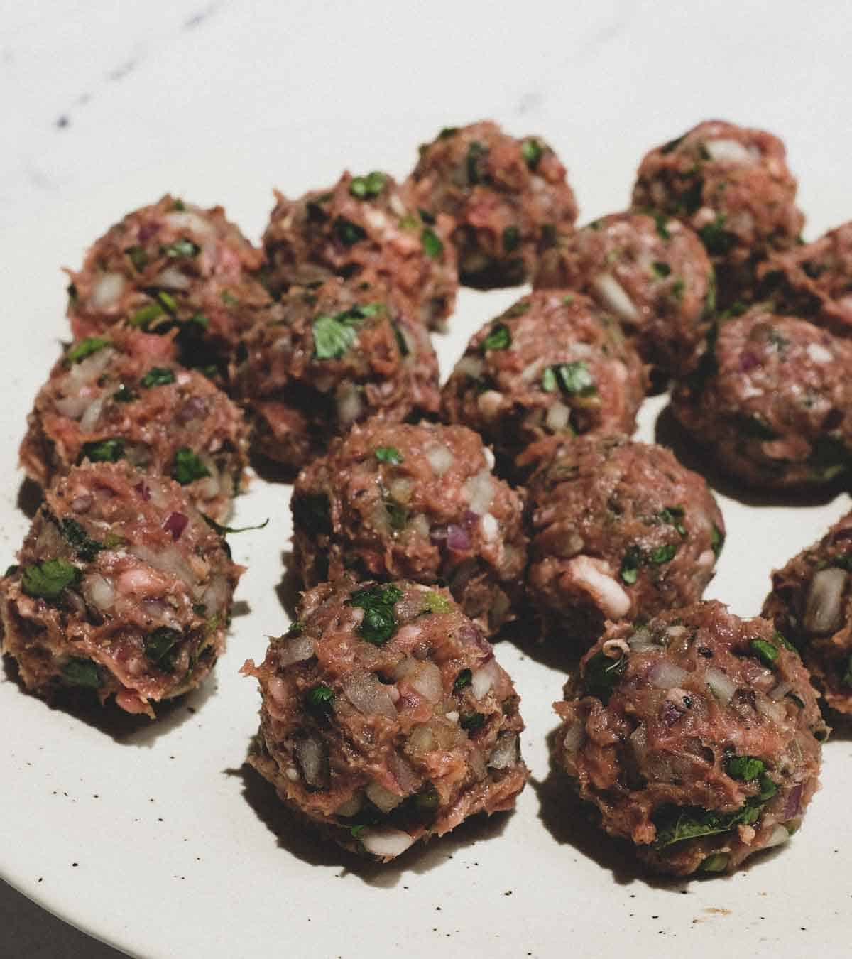 Moroccan Kefta (meatballs) rolled and placed on a plate before cooking.