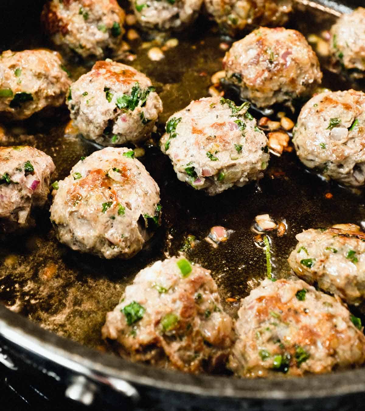 Moroccan Kefta (meatballs) frying in a large pan until browned on all sides.