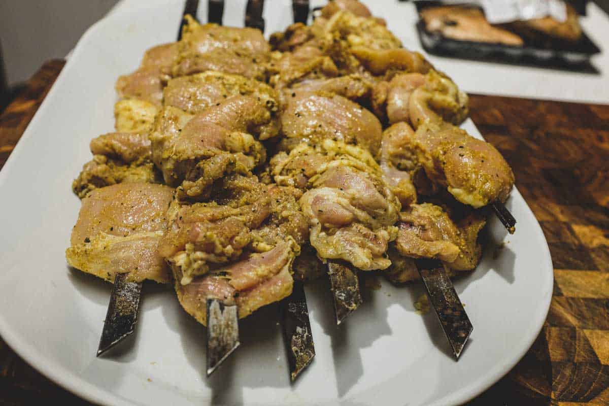 Chicken skewers on a platter marinating in Middle Eastern spices.