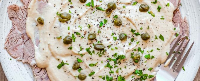 A large platter of Italian Vitello Tonnato (veal slices with a tuna mayonnaise) garnished with parsley and capers.