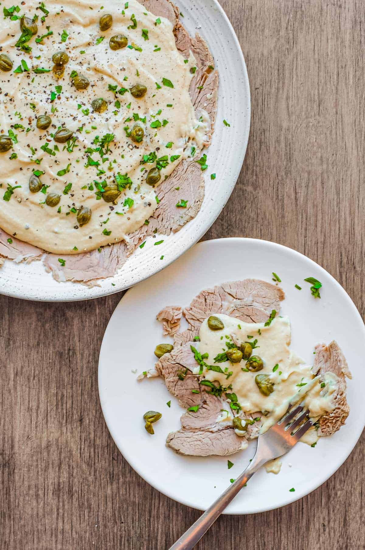 A small plate of Italian Vitello Tonnato (veal slices with a tuna mayonnaise) sits alongside a larger platter.