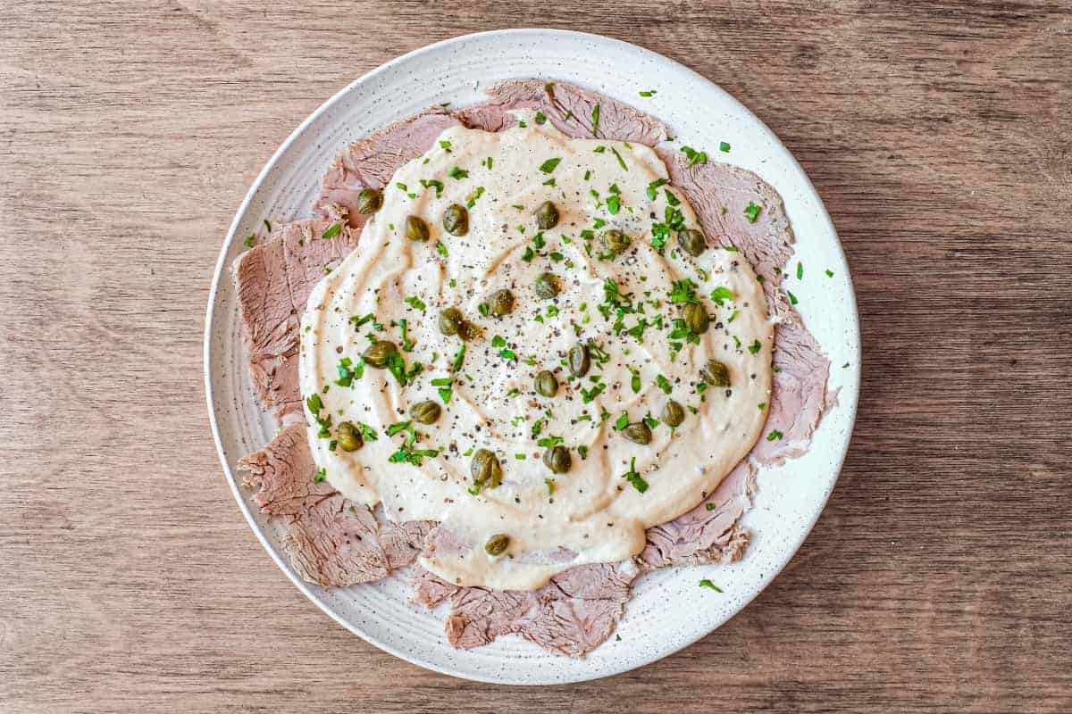 A large platter of Italian Vitello Tonnato (veal slices with a tuna mayonnaise) garnished with parsley and capers.