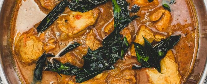 Achari Chicken curry with fried curry leaves in a silver bowl