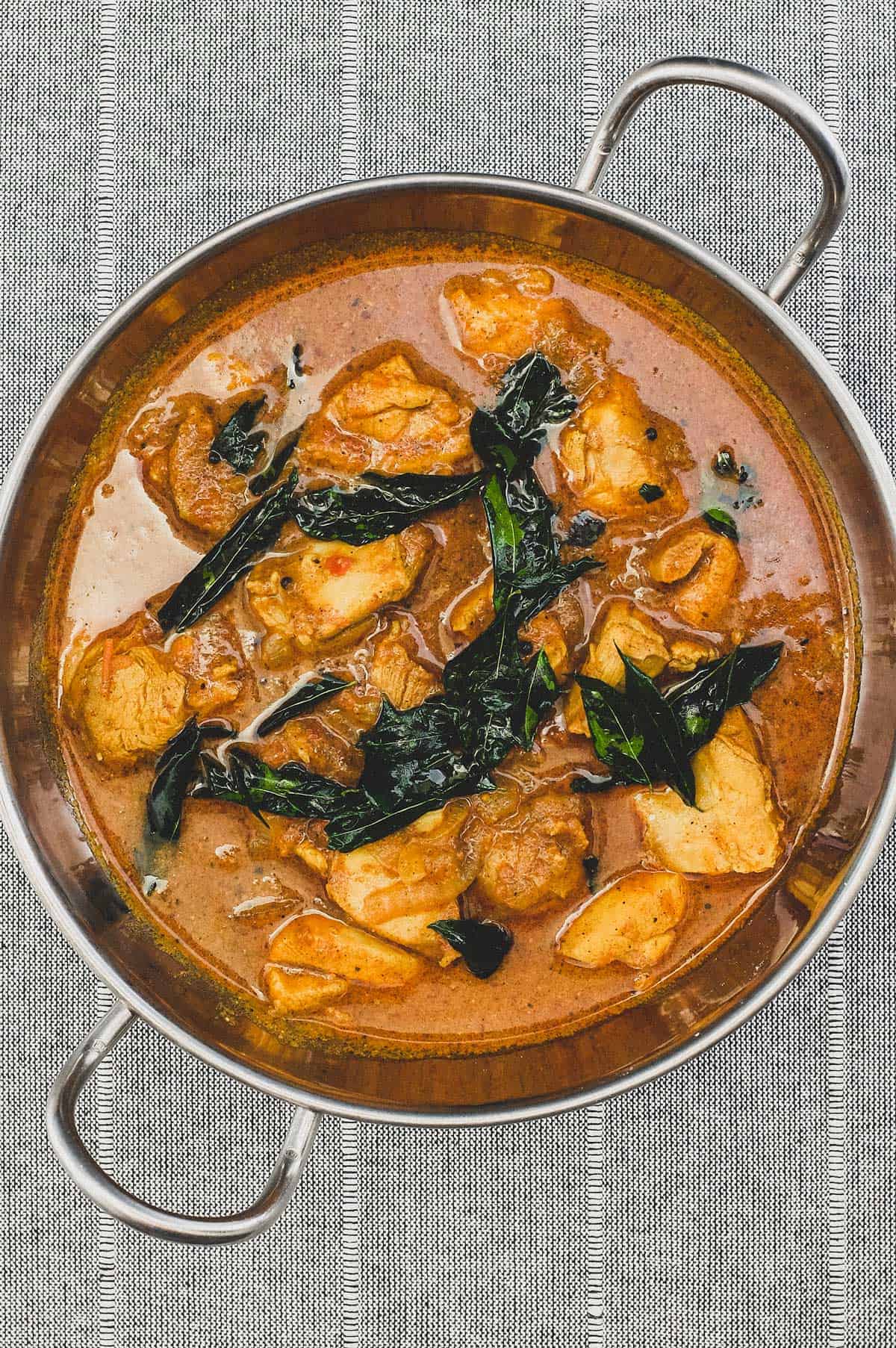 Achari Chicken curry with fried curry leaves in a silver bowl