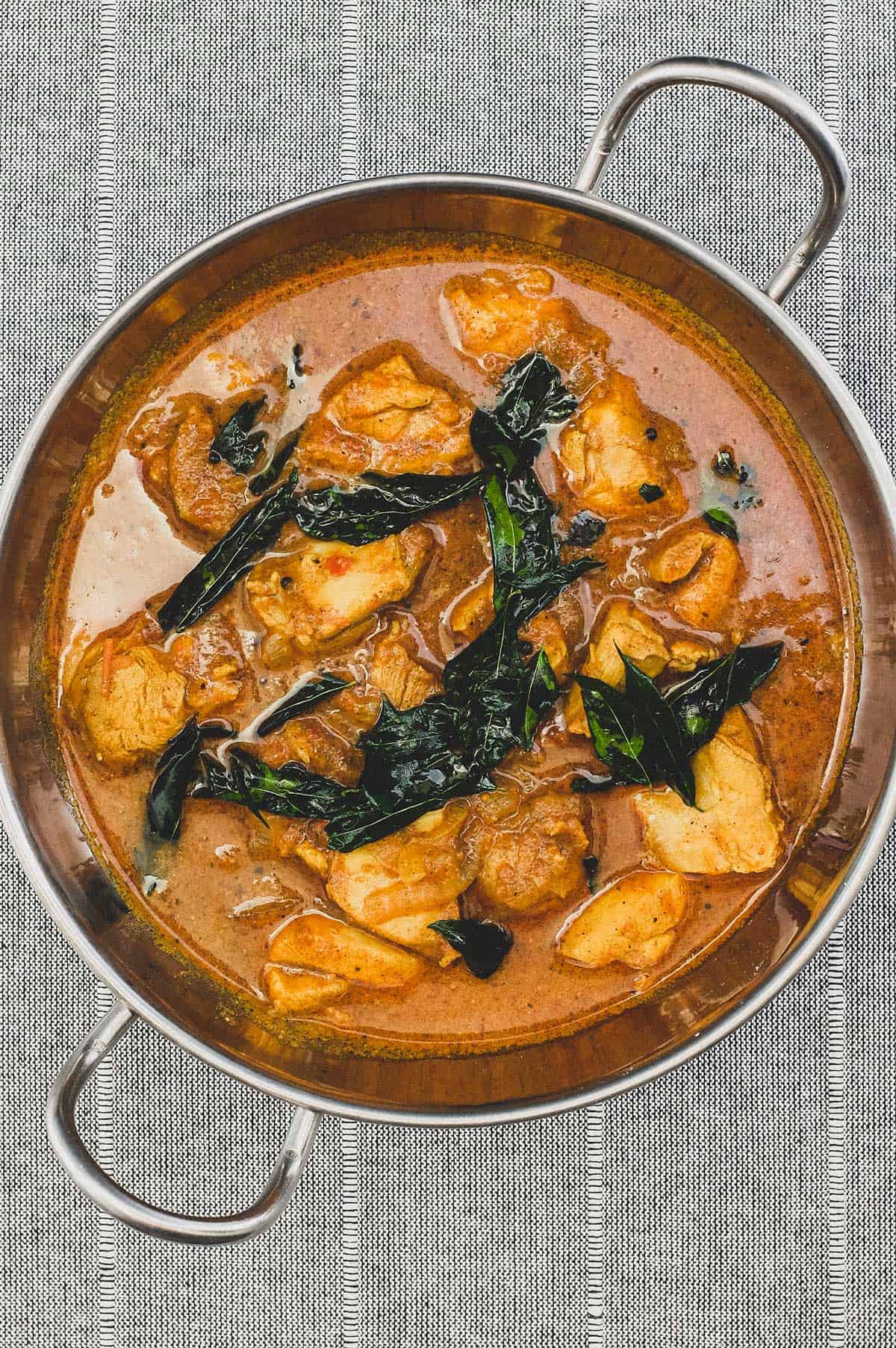 Achari Chicken curry with fried curry leaves in a silver bowl