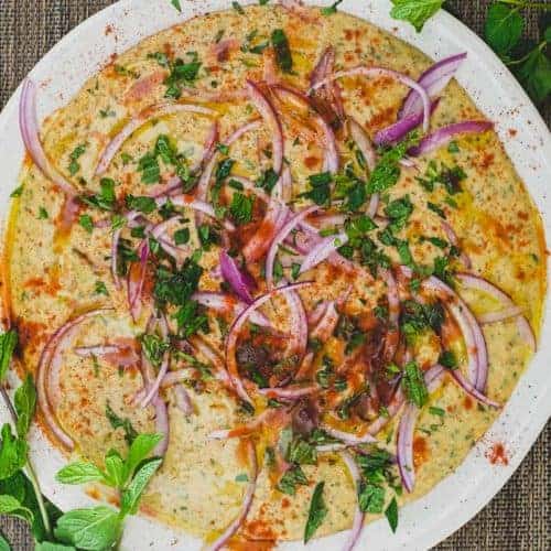 A bowl of Bessara scattered with vegetables, herbs and more