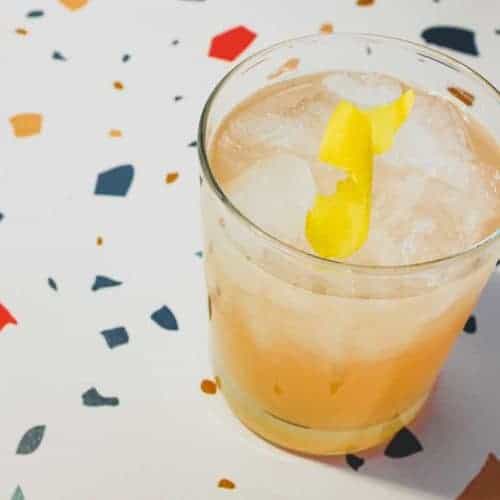 A highball glass with a Pamplemousse Cocktail on a stylish terrazzo surface. A twist of lemon rind sits on top.