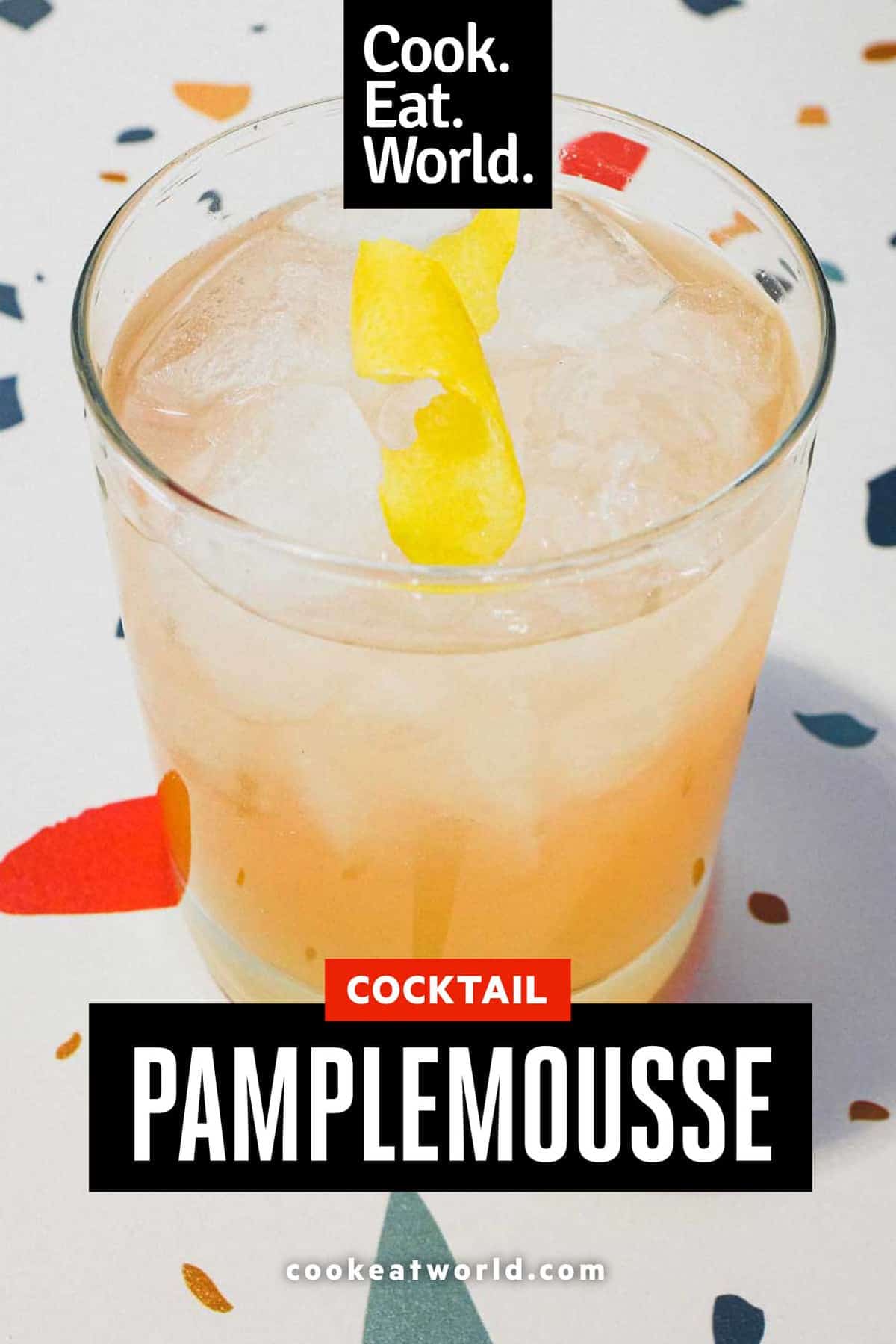 A highball glass with a Pamplemousse Cocktail on a stylish terrazzo surface. A twist of lemon rind sits on top.