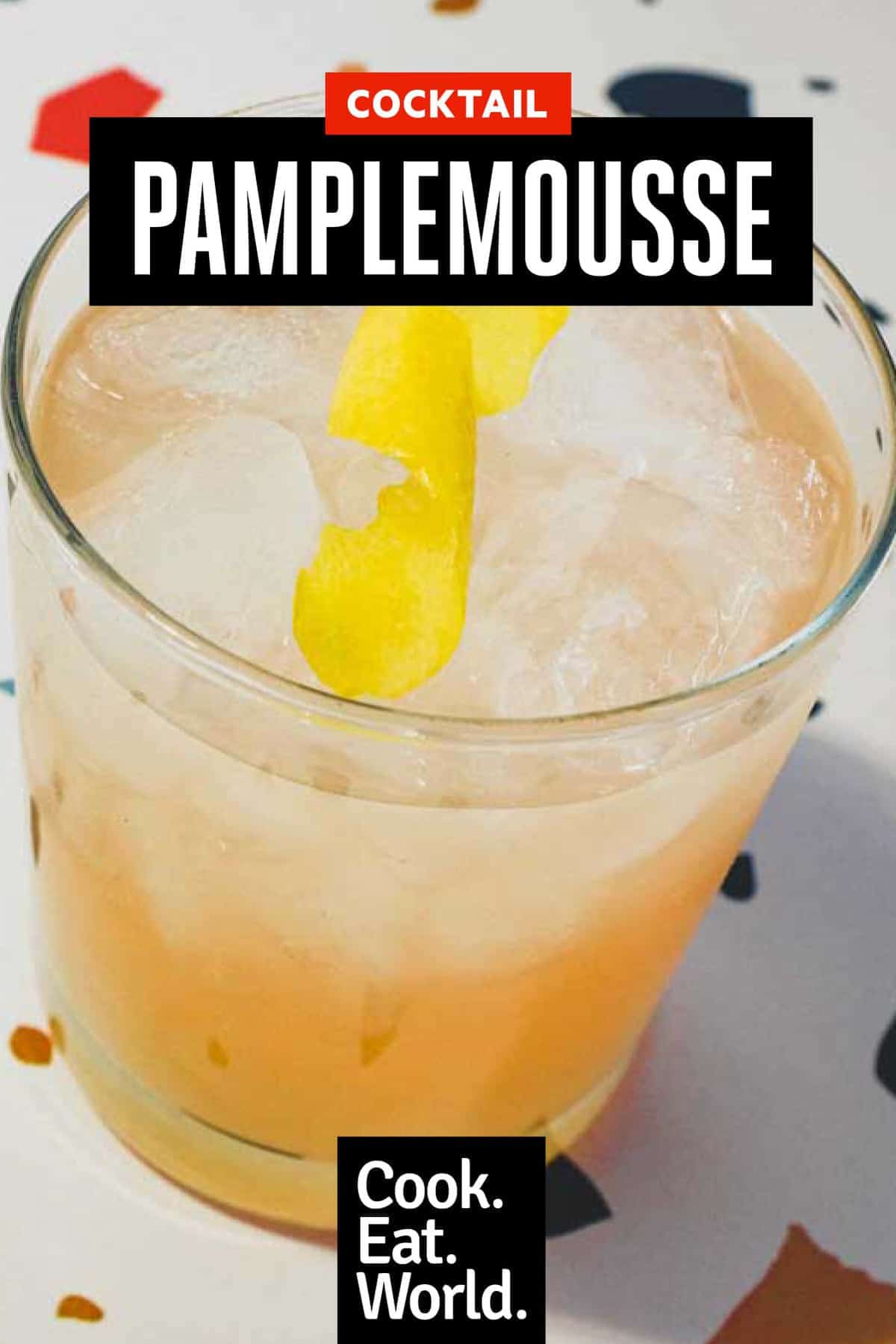 A highball glass with a Pamplemousse Cocktail on a stylish terrazzo surface. A twist of lemon rind sits on top.