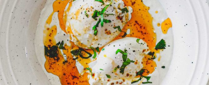 A small bowl of Turkish Cilbir (poached eggs) drizzled in orange Aleppo pepper butter