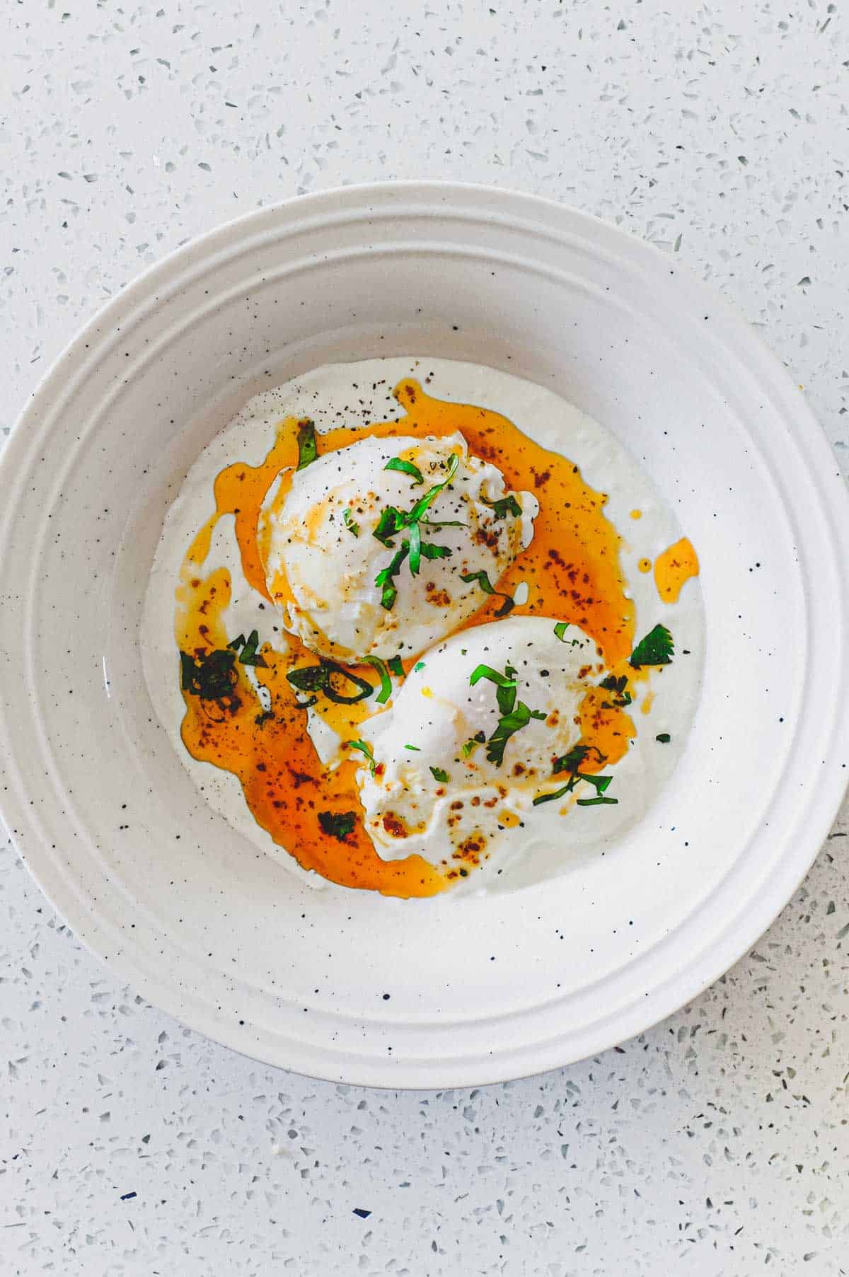 A small bowl of Turkish Cilbir (poached eggs) drizzled in orange Aleppo pepper butter