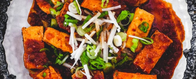 Fried tofu is lightly braised in Korean chilli (gochugaru) and topped with radish and spring onion