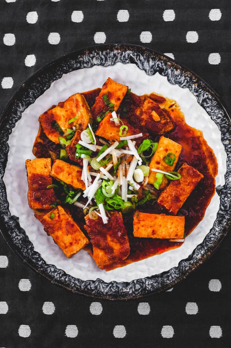 Fried tofu is lightly braised in Korean chilli (gochugaru) and topped with radish and spring onion