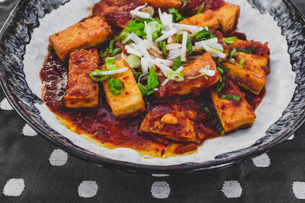 Fried tofu is lightly braised in Korean chilli (gochugaru) and topped with radish and spring onion