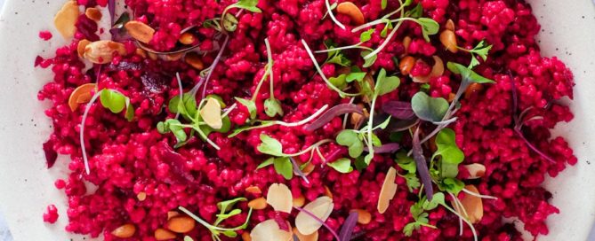 Israeli Couscous with Beetroot on a plate, scattered with micro greens and nuts.