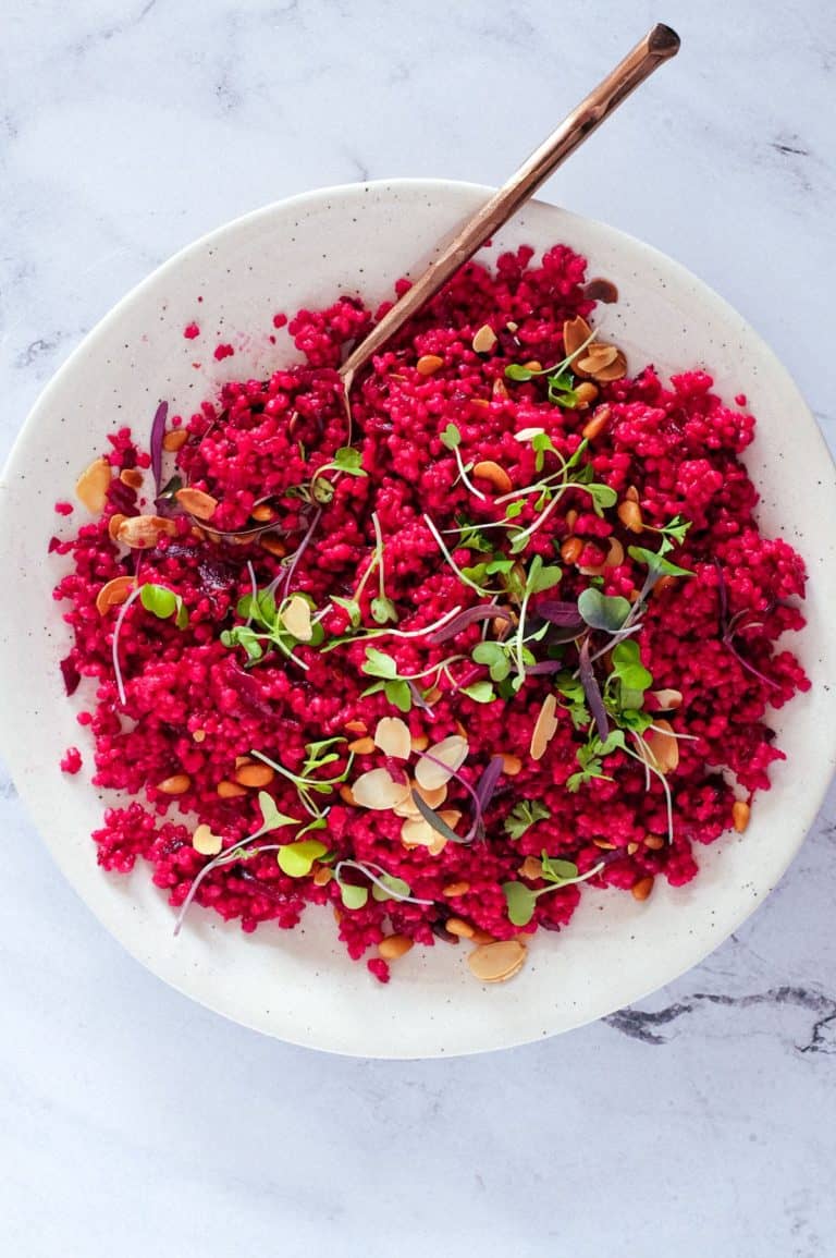 Israeli Couscous with Beetroot on a plate, scattered with micro greens and nuts.