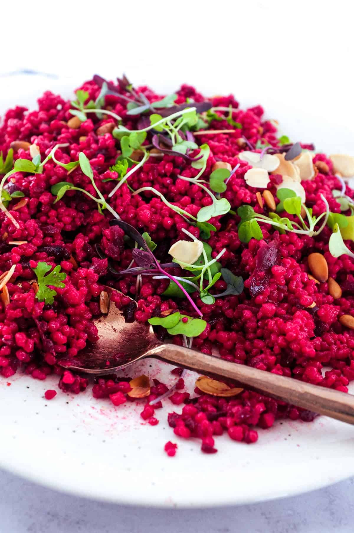 Israeli Couscous with Beetroot on a plate, scattered with micro greens and nuts.