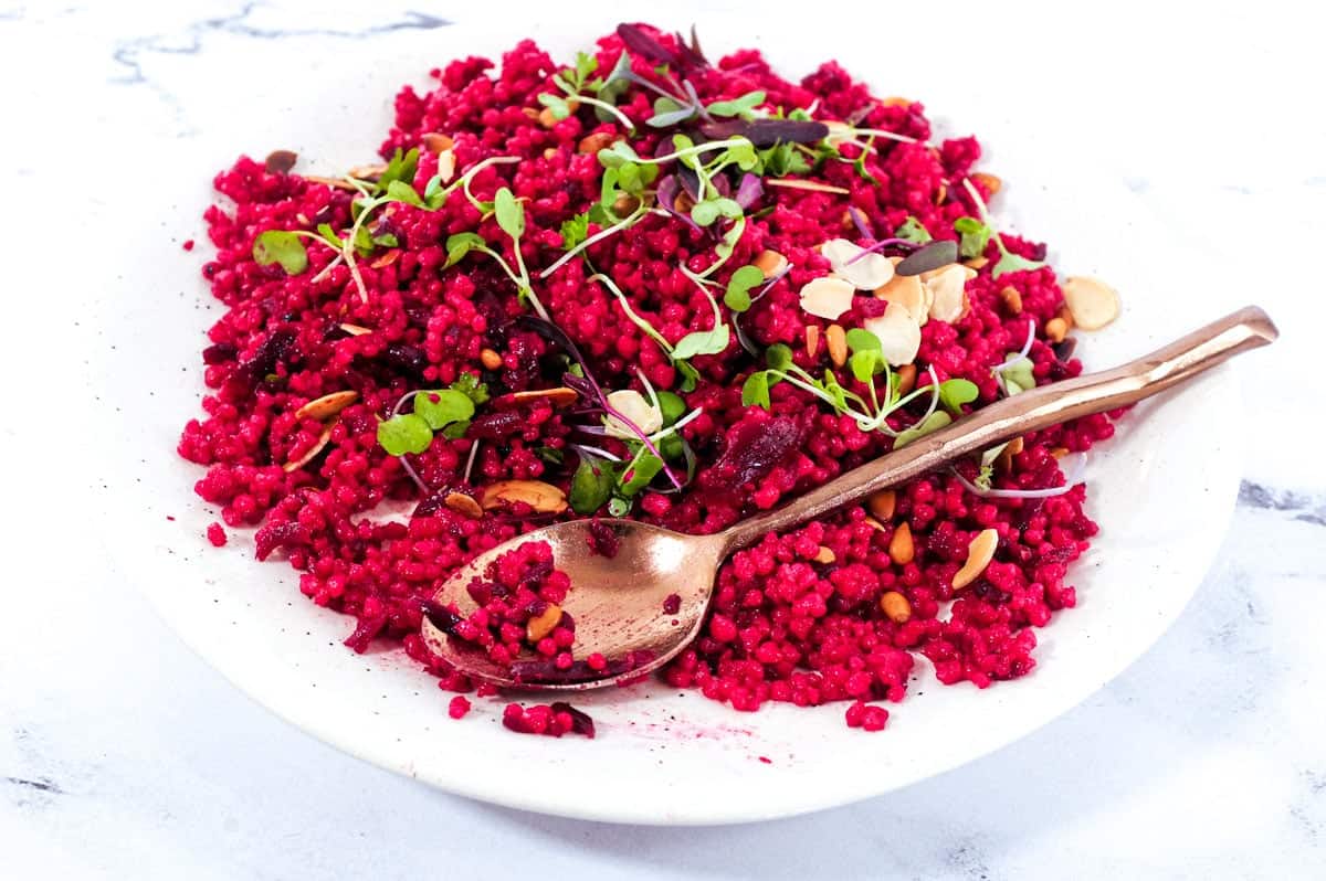 Israeli Couscous with Beetroot on a plate, scattered with micro greens and nuts.