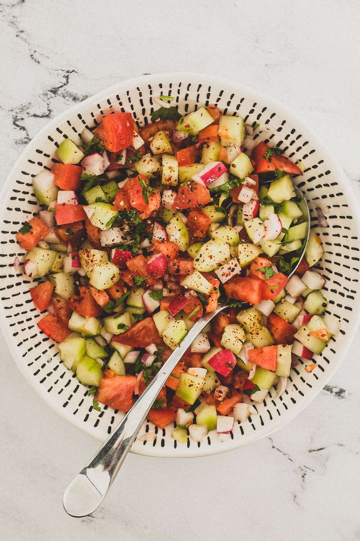 Cucumber, tomato & red onion are combined with a little cilantro and lime juice and served in a bowl as a chopped salad for Indian food.