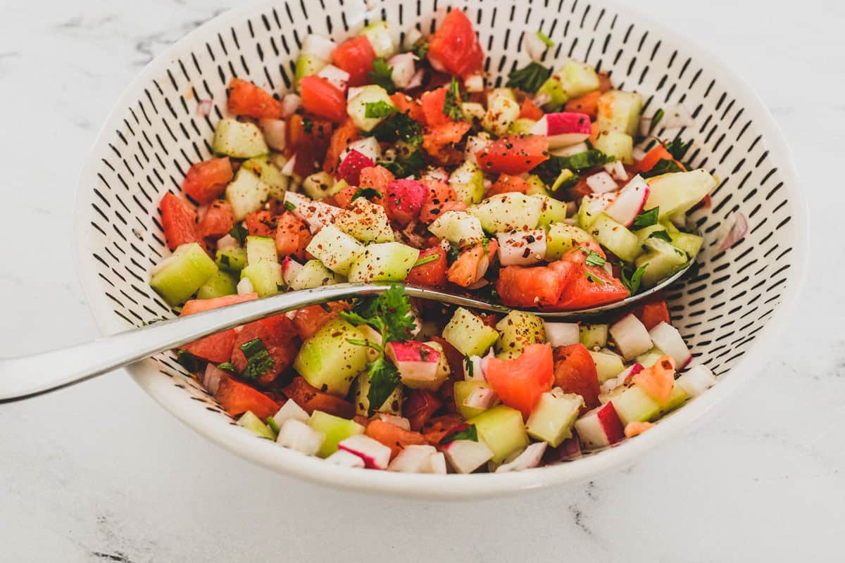 Cucumber, tomato & red onion are combined with a little cilantro and lime juice and served in a bowl as a chopped salad for Indian food.