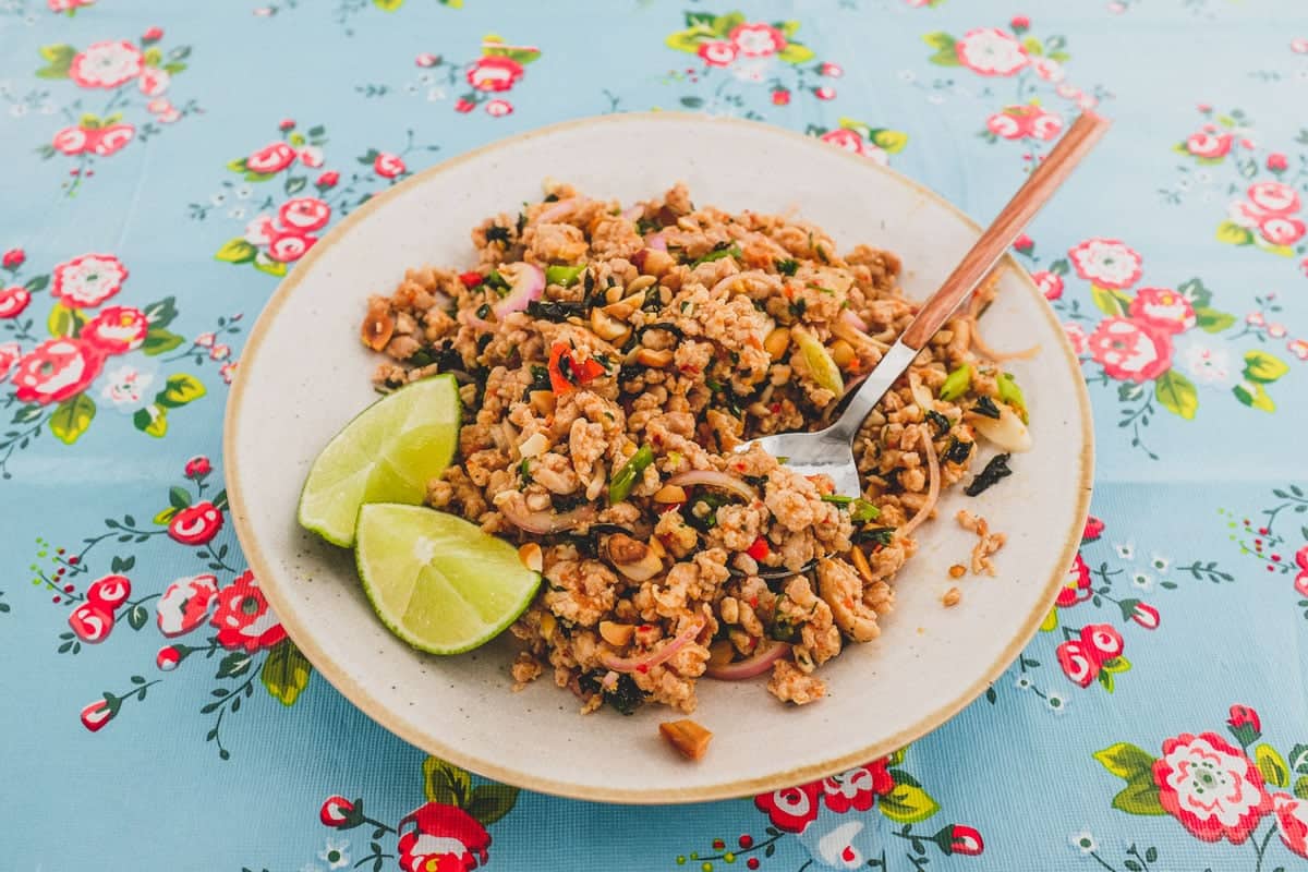 Ground chicken combined with Laotian aromatics and spices to a form a dry, spicy chicken salad. The platter sits on a colourful, floral tablecloth - like the kind you find in South East Asian markets.