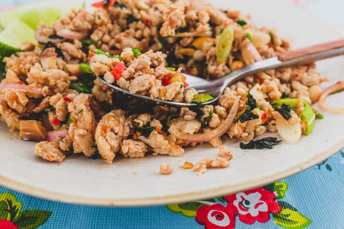 Ground chicken combined with Laotian aromatics and spices to a form a dry, spicy chicken salad. The platter sits on a colourful, floral tablecloth - like the kind you find in South East Asian markets.