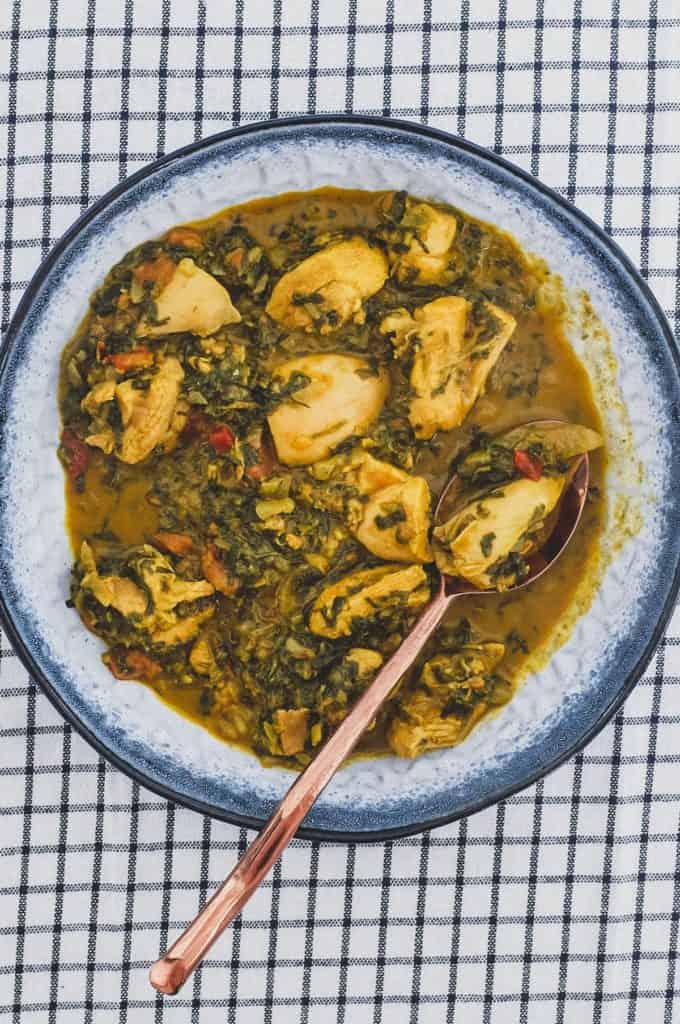 A bowl of chicken curry cooked with fenugreek leaves with a serving spoon