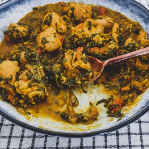A bowl of chicken curry cooked with fenugreek leaves with a serving spoon
