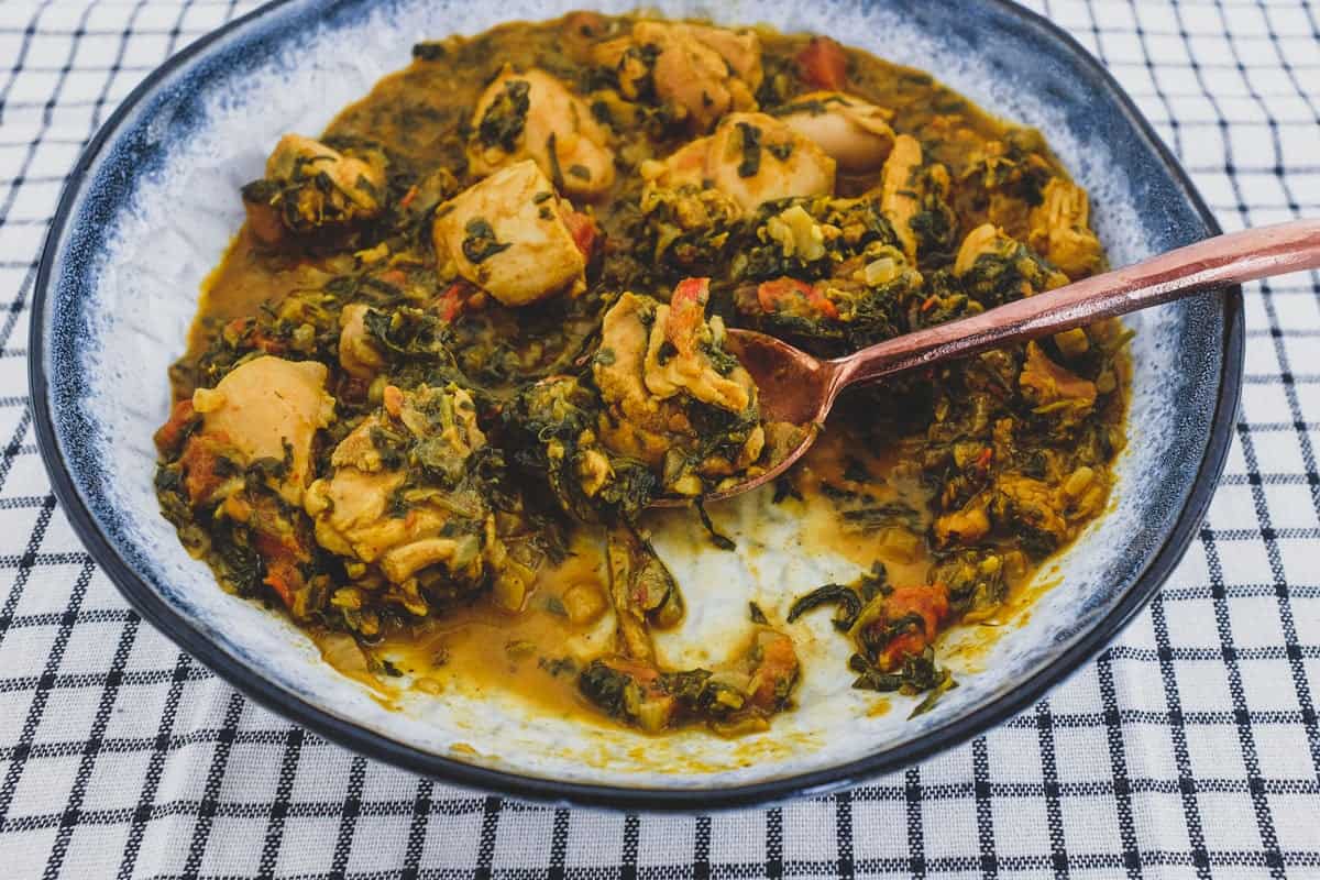 A bowl of chicken curry cooked with fenugreek leaves with a serving spoon