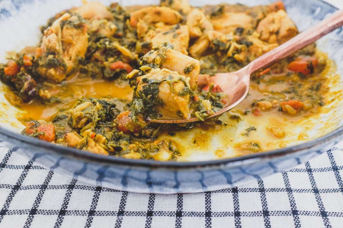 A bowl of chicken curry cooked with fenugreek leaves with a serving spoon