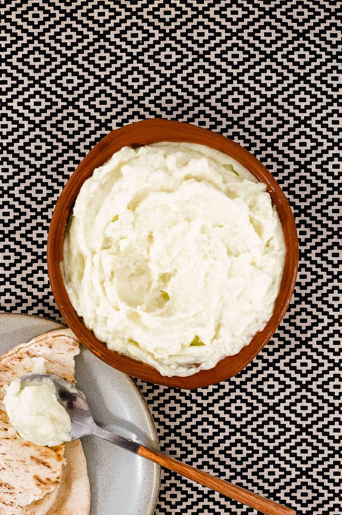 A bowl of Toum (garlic mayonnaise) alongside some flatbreads and a spoon.