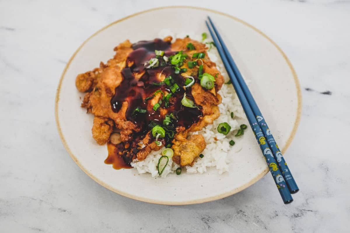 A plate of chicken egg foo young with gravy ion a platter with rice and chopsticks