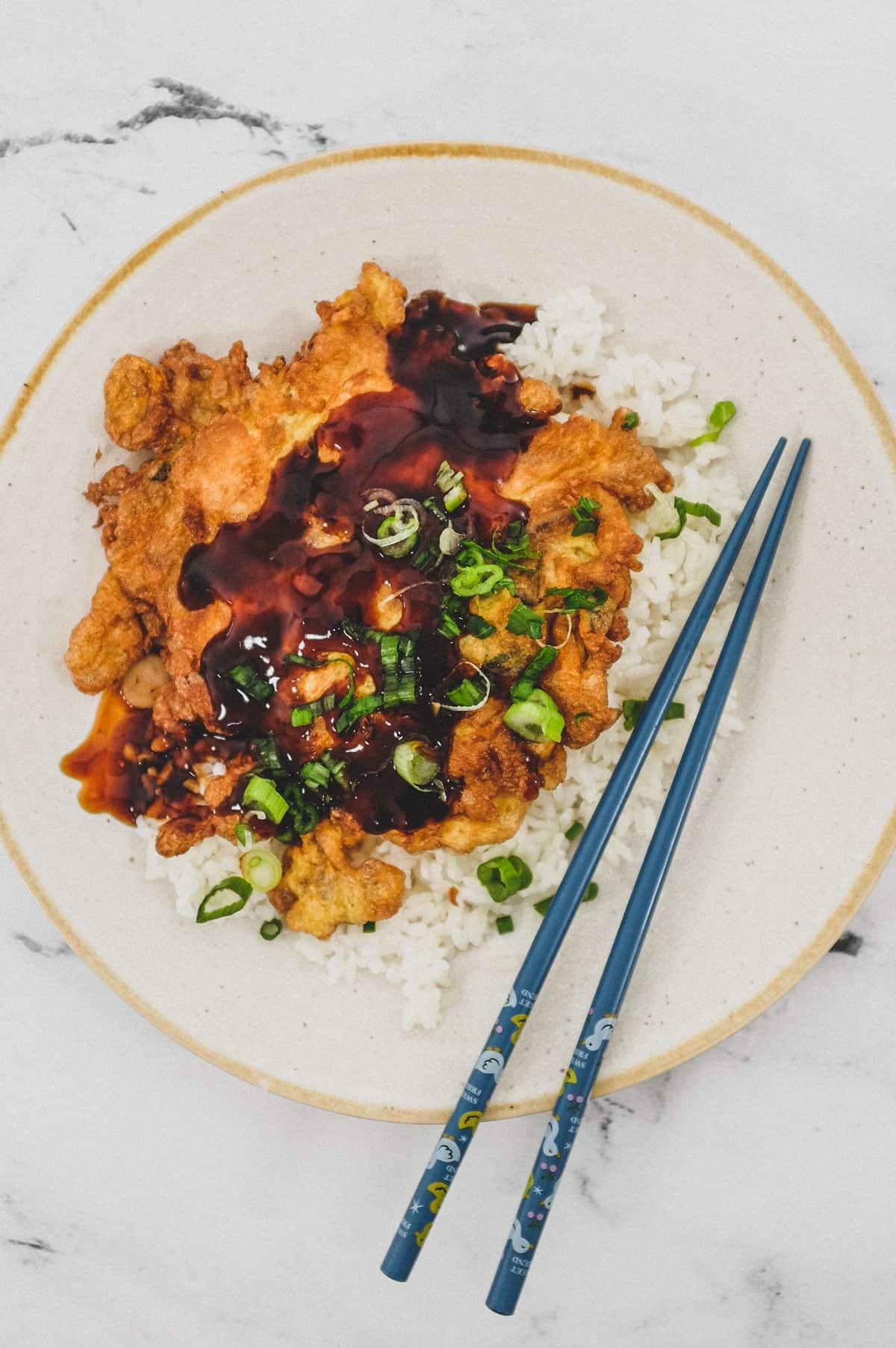 A plate of chicken egg foo young with gravy ion a platter with rice and chopsticks