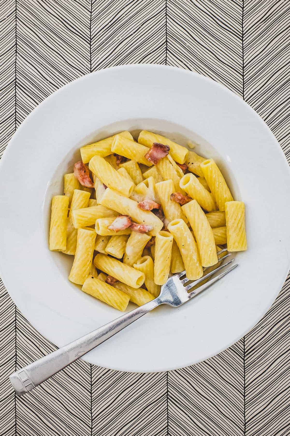 Rigatoni tubes in a bowl with Guanciale pork cheek and pecorino romano cheese