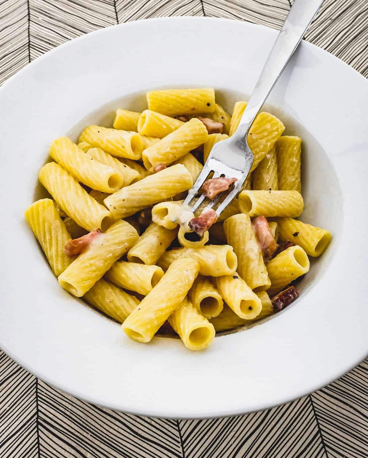 Rigatoni tubes in a bowl with Guanciale pork cheek and pecorino romano cheese