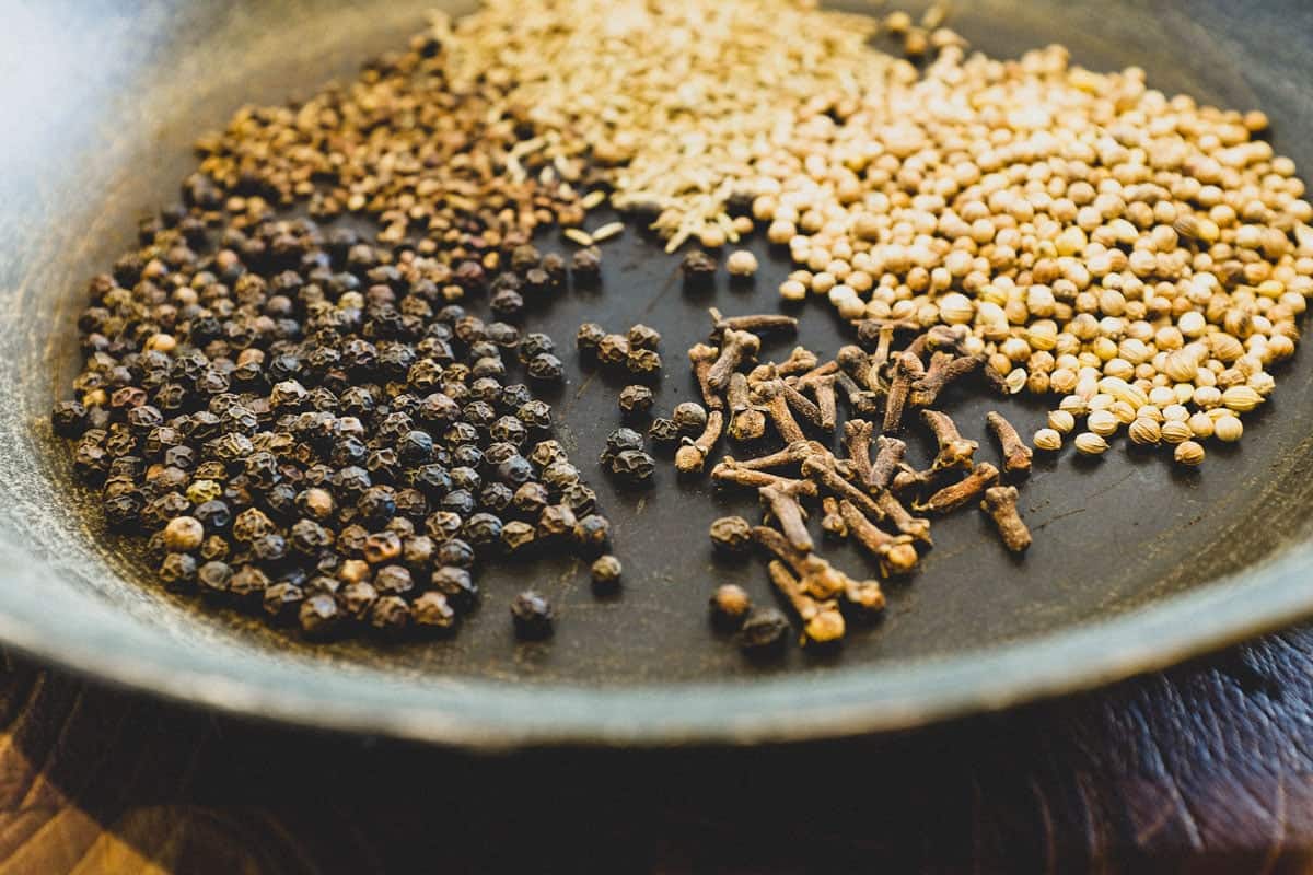 A pan with Black peppercorns, cloves, coriander, cardamom and cumin.