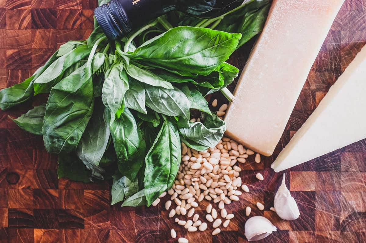 Ingredients for pesto Genovese: basil, olive oil, Pecorino cheese, parmigiana Reggiano cheese, pine nuts and garlic sit on a wooden board