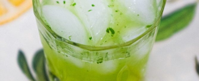 A green cocktail made from Gin and Thai Basil sits on a tablecloth of citrus fruits
