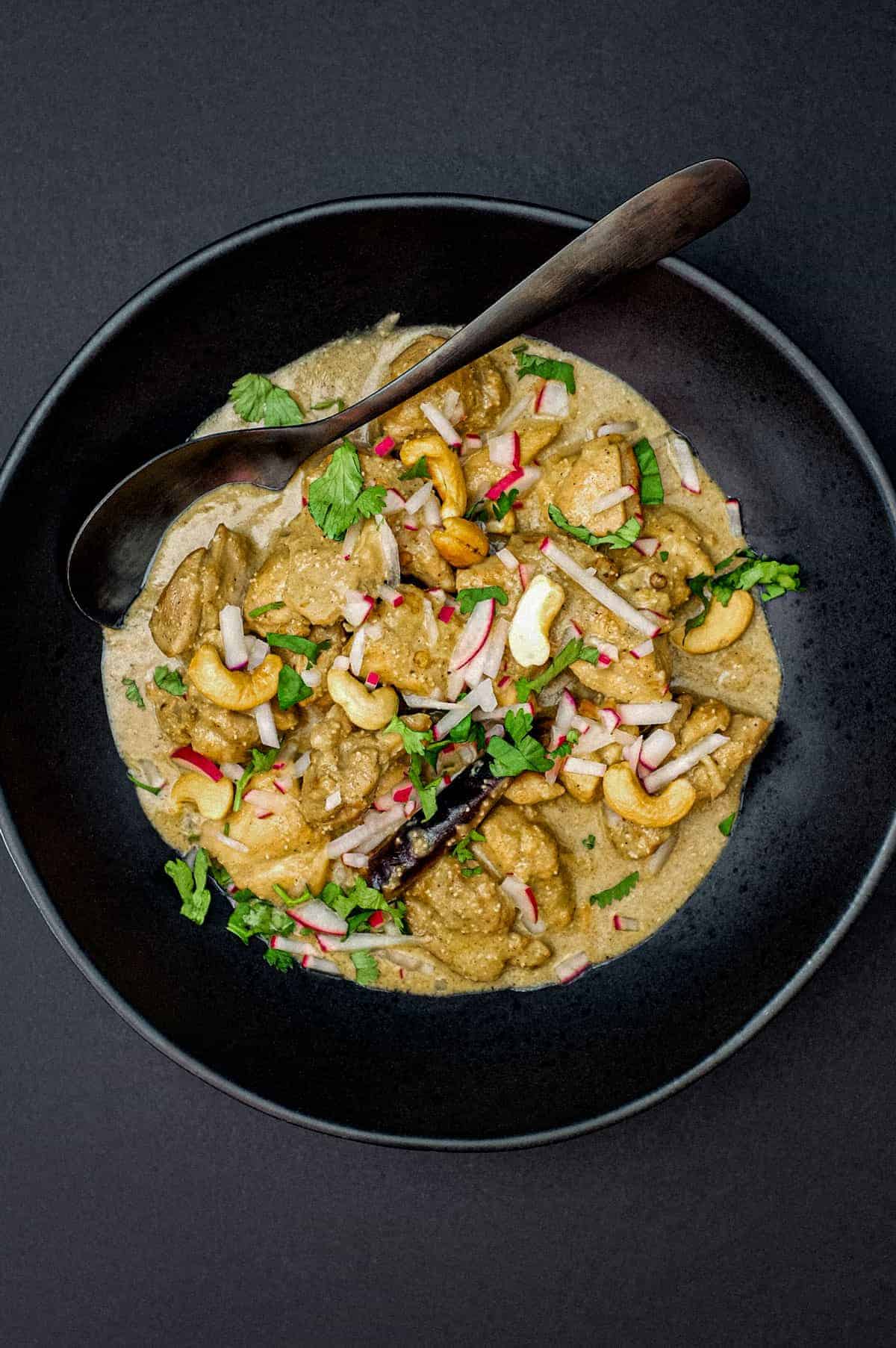 Bengali Rezala Chicken in a black bowl with spoon on a black background.