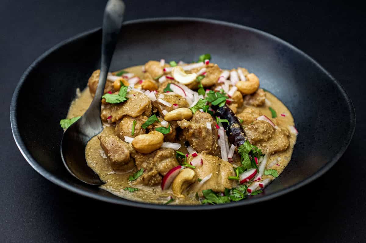 Bengali Rezala Chicken in a black bowl with spoon on a black background.