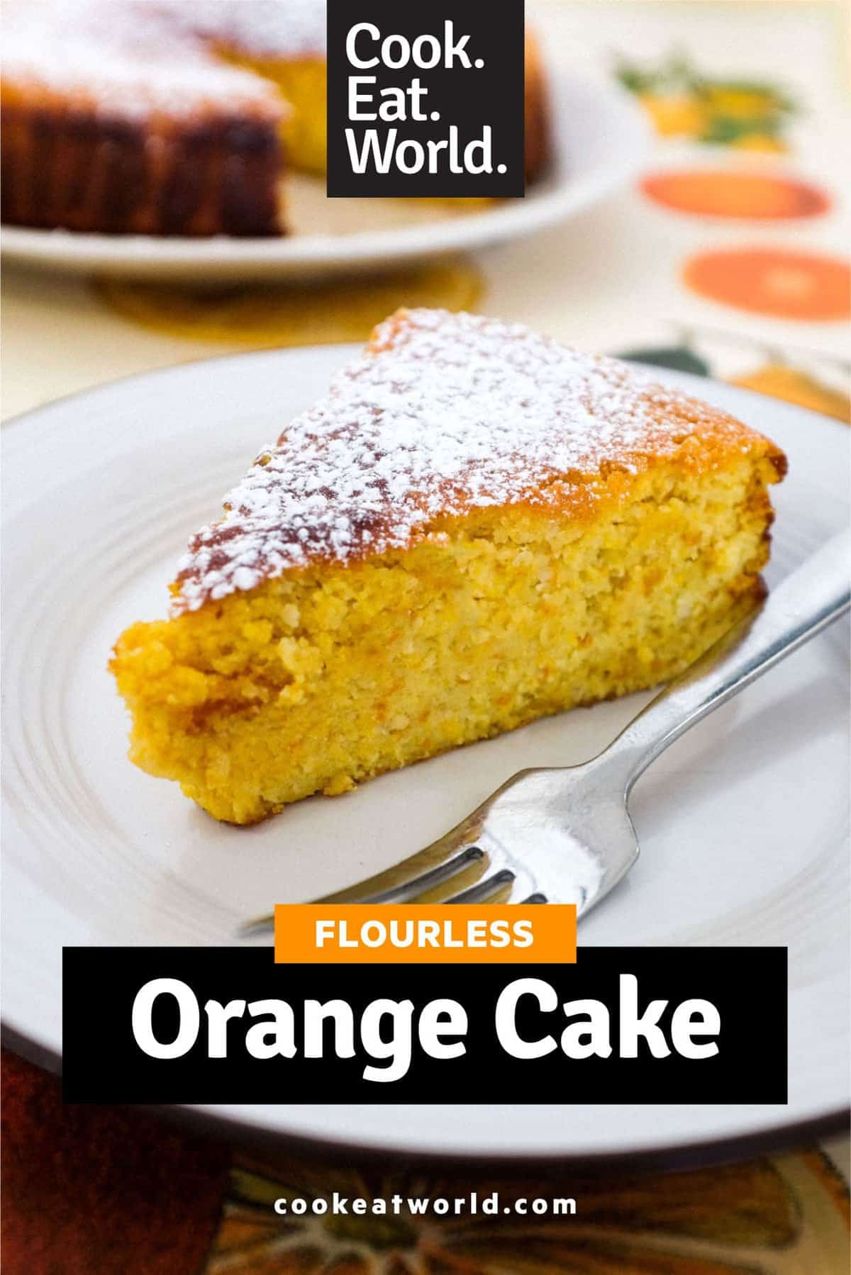 A flourless orange cake, dusted with icing sugar, sits in the foreground with a slice taken out of it. The slice of cake sits in the background out of focus.