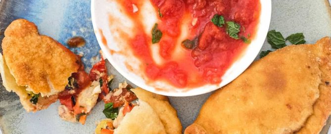 A plate with two mini calzone pizza (Panzerotti) stuffed with tuna & red peppers sit on a plate with some tomato dipping sauce.