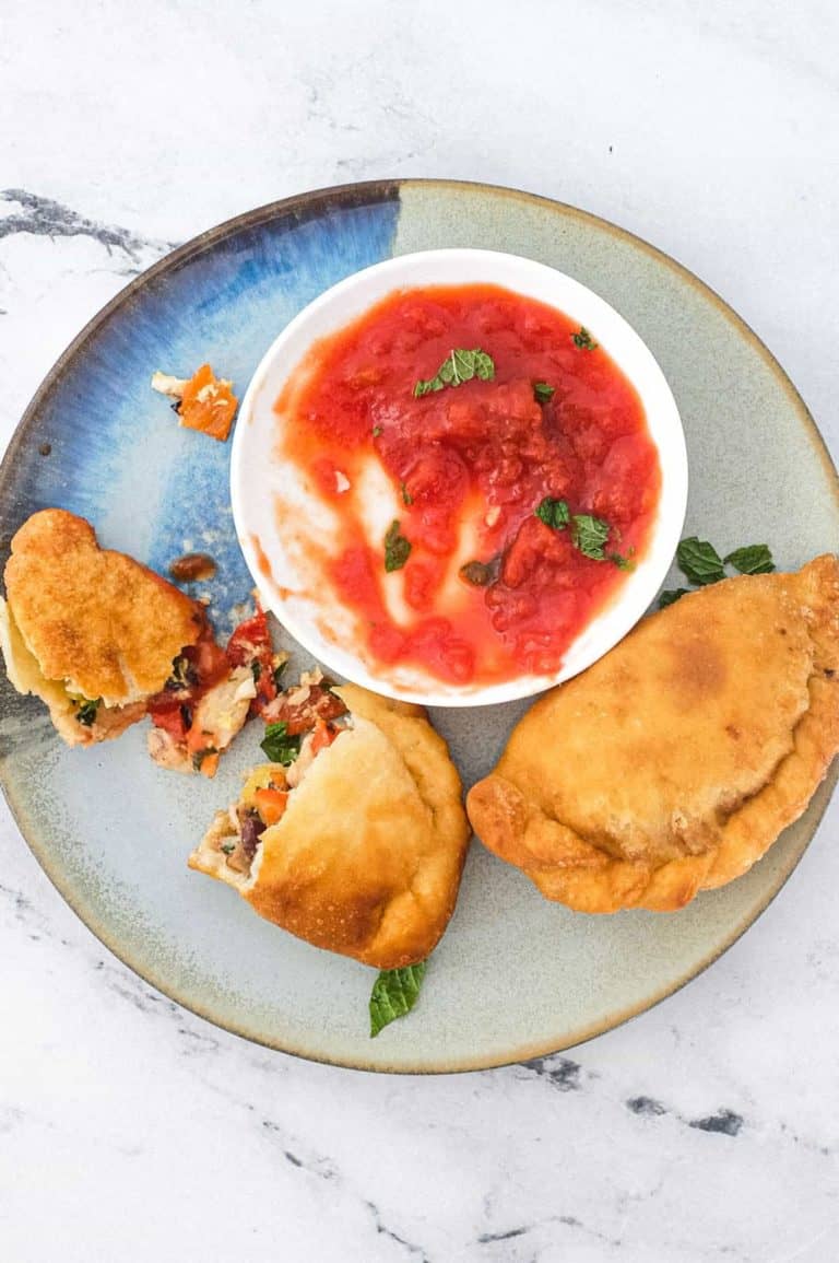 A plate with two mini calzone pizza (Panzerotti) stuffed with tuna & red peppers sit on a plate with some tomato dipping sauce.
