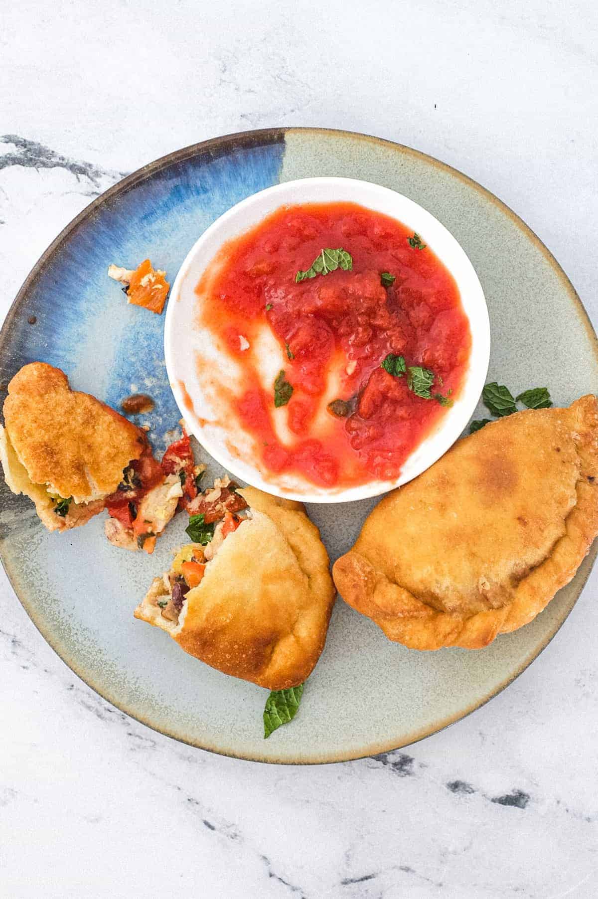 A plate with two mini calzone pizza (Panzerotti) stuffed with tuna & red peppers sit on a plate with some tomato dipping sauce.