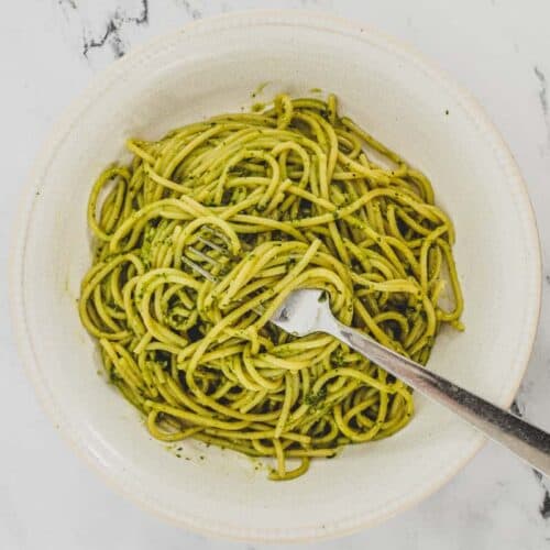 A bowl of Spaghetti with Pesto Genovese. A fork twists around a few noodles.