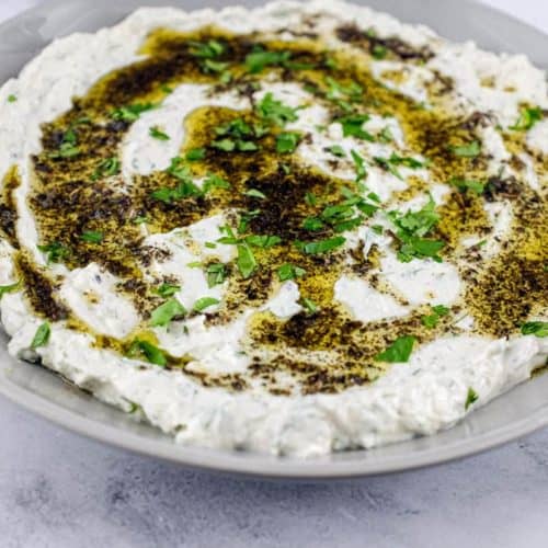 A plate of Haydari yoghurt dip, drizzled with olive oil and dried mint with a large copper spoon sit on a marble tabletop